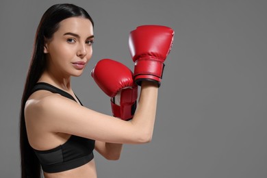 Photo of Beautiful woman in boxing gloves training on grey background. Space for text