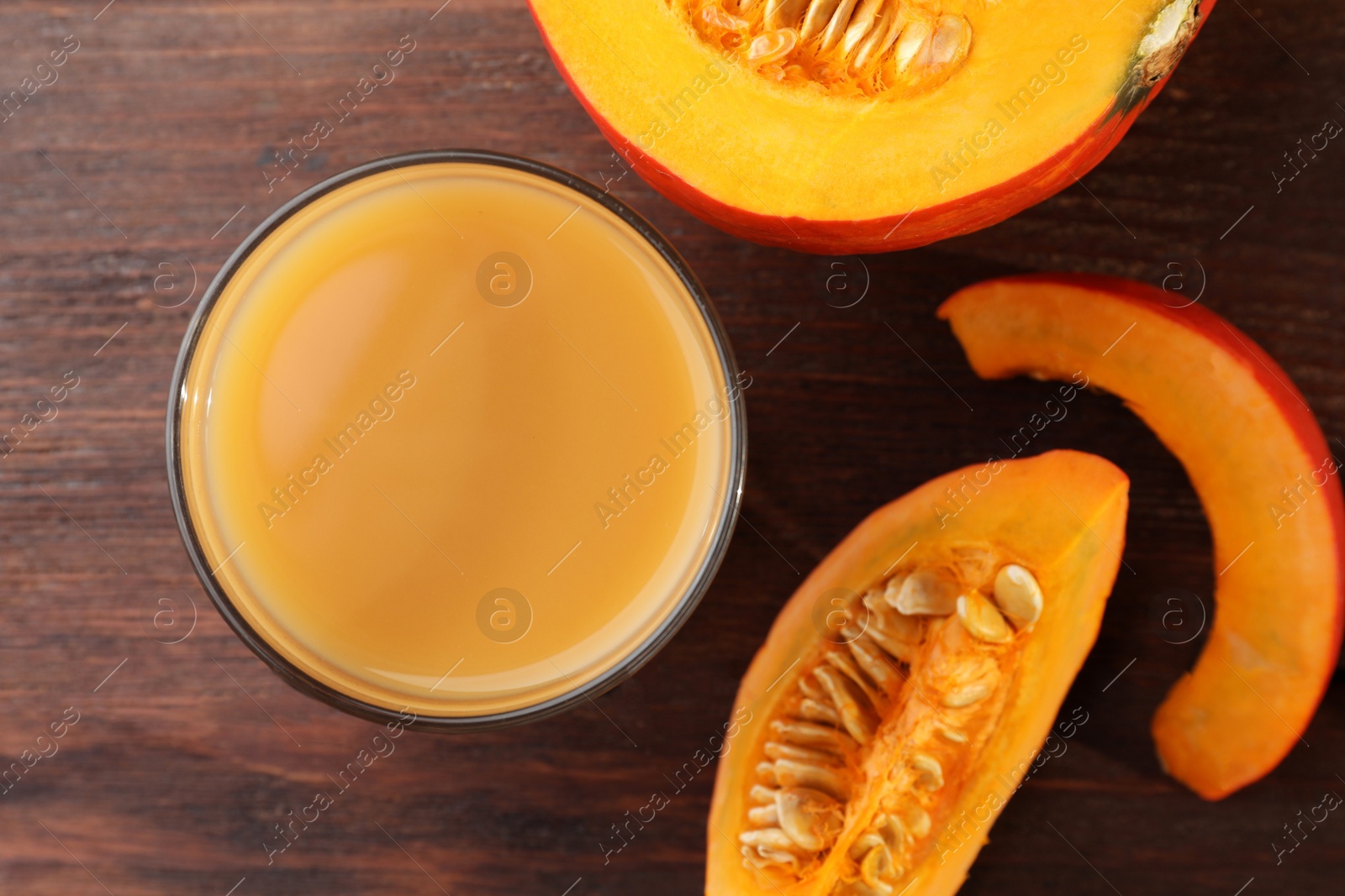Photo of Tasty pumpkin juice in glass and cut pumpkin on wooden table, flat lay