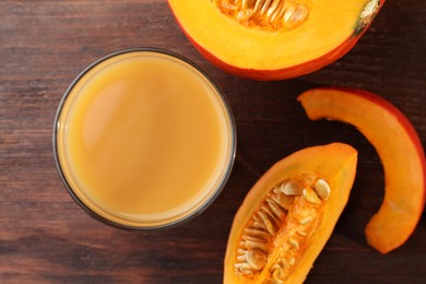 Photo of Tasty pumpkin juice in glass and cut pumpkin on wooden table, flat lay