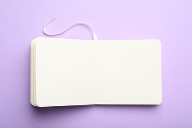 Stylish open notebook on lilac background, top view