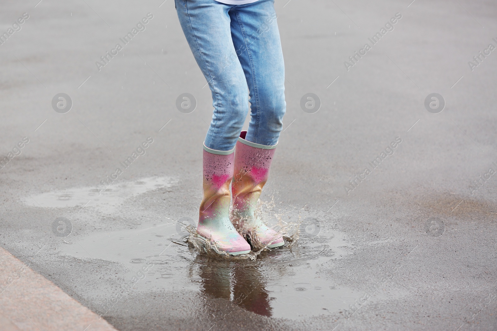 Photo of Woman jumping in rubber boots under rain on street, closeup