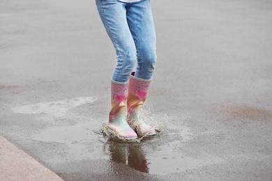 Woman jumping in rubber boots under rain on street, closeup