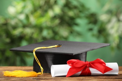 Graduation hat and diploma on wooden table against blurred background, space for text