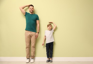 Father and son comparing their heights near light wall indoors. Space for text