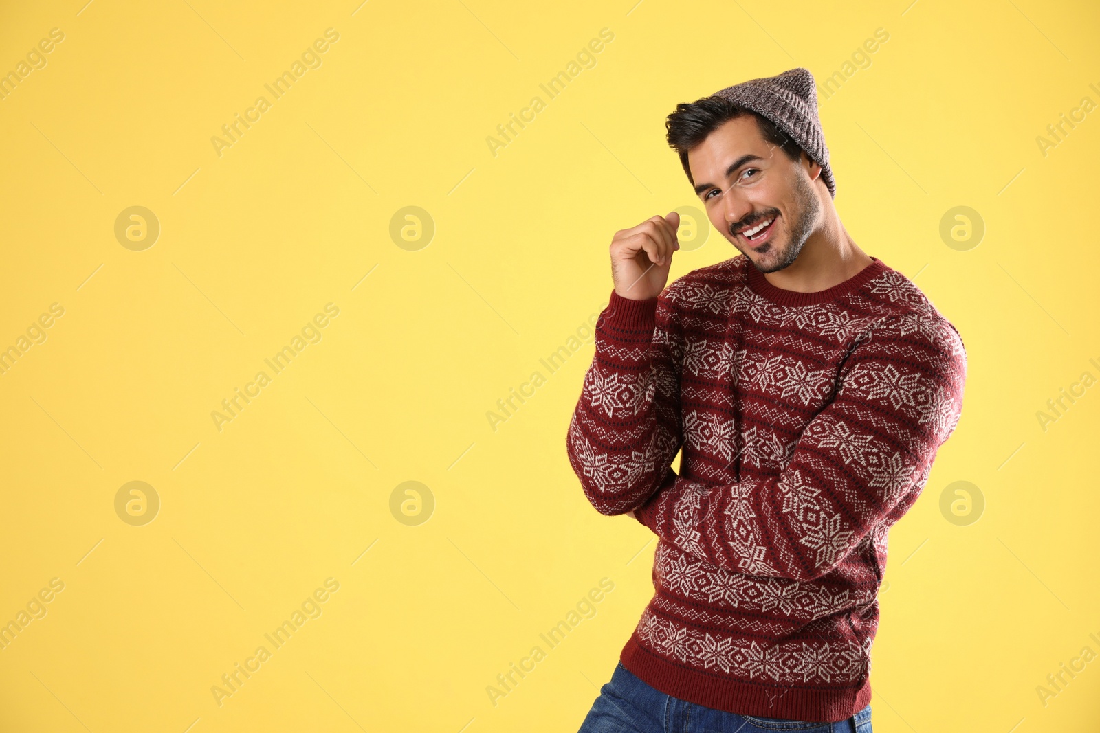 Photo of Portrait of young man in Christmas sweater and hat on yellow background. Space for text