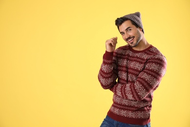 Photo of Portrait of young man in Christmas sweater and hat on yellow background. Space for text