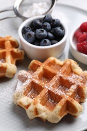 Photo of Delicious Belgian waffles with fresh berries and powdered sugar on plate, closeup