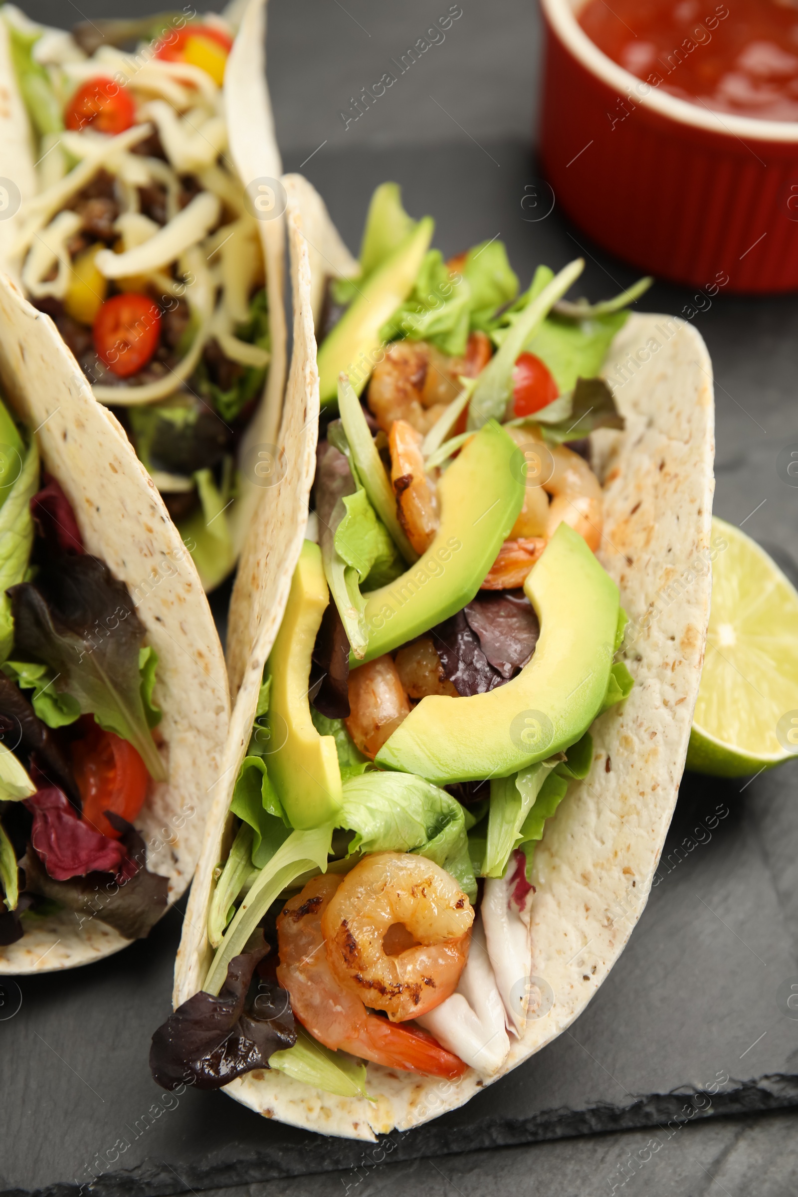 Photo of Delicious tacos with shrimps and avocado on black table, closeup