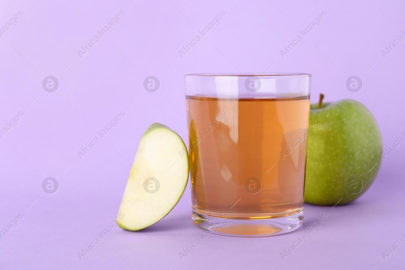 Photo of Glass of juice and apples on violet background