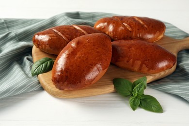 Photo of Delicious baked pirozhki and basil on white wooden table, closeup