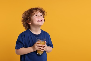 Photo of Cute little boy with glass of fresh juice on orange background, space for text