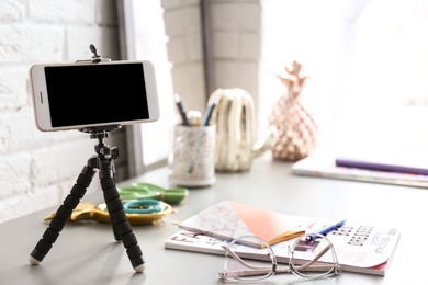 Photo of Tripod with modern phone on table. Blogger concept