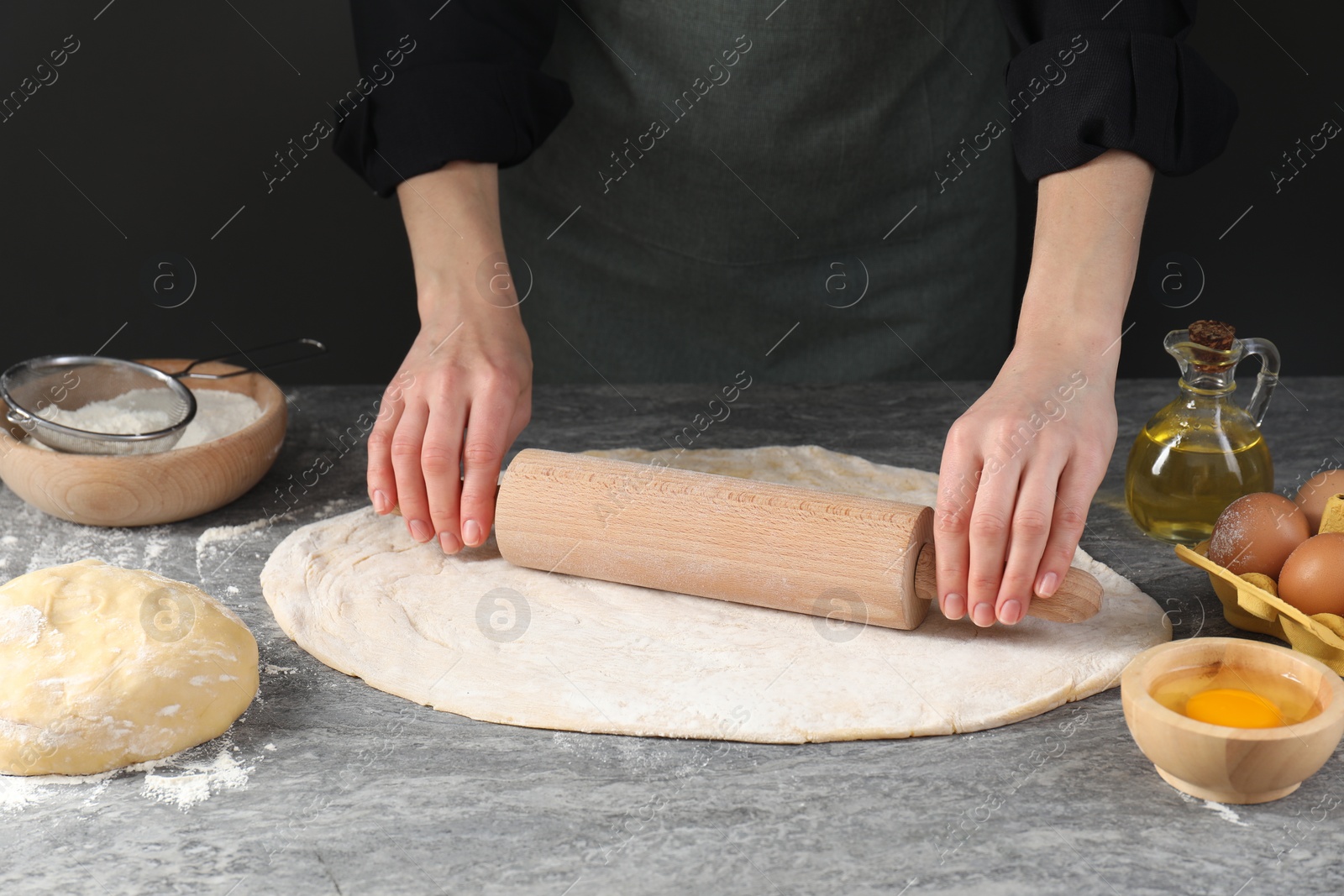 Photo of Woman rolling raw dough at grey table, closeup