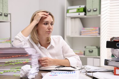 Photo of Overwhelmed woman at table with many documents in office