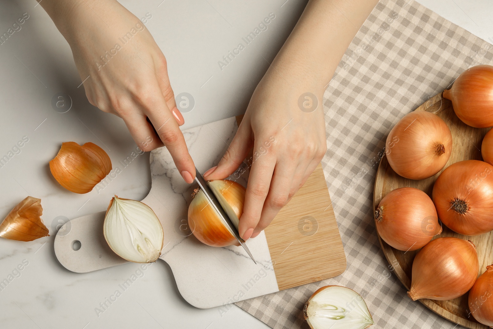 Photo of Woman cutting ripe onion at white marble table, top view