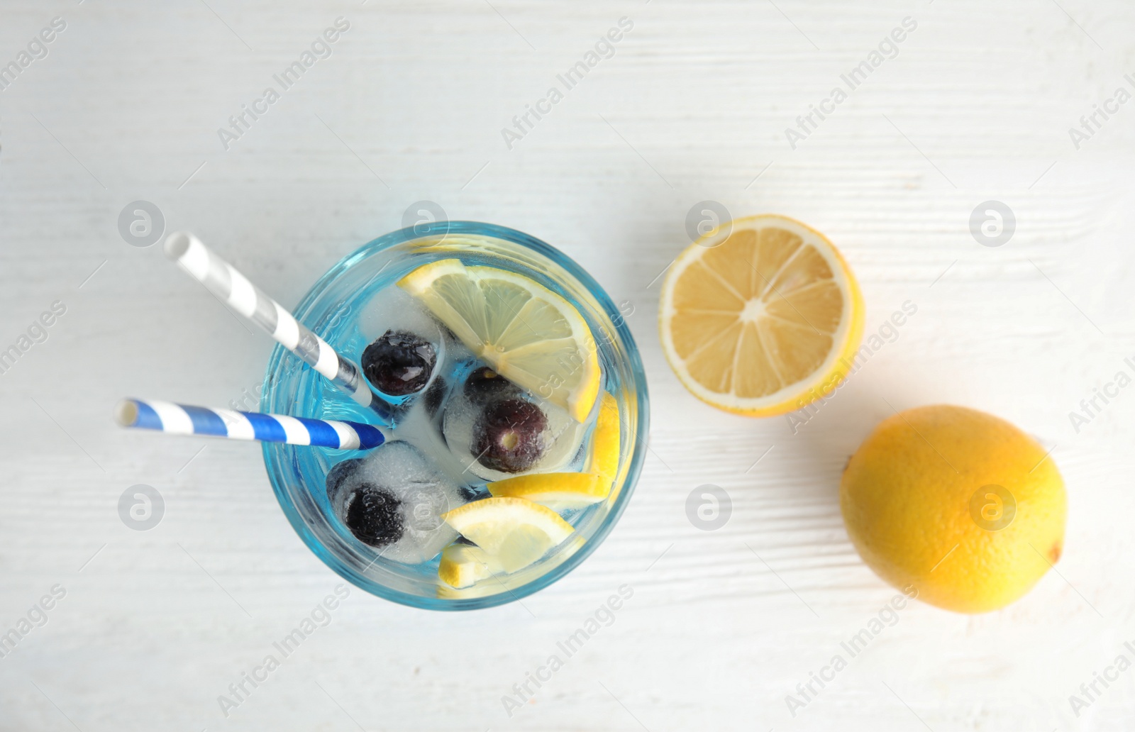 Photo of Tasty cocktail with blueberry ice cubes and lemons on wooden background, top view