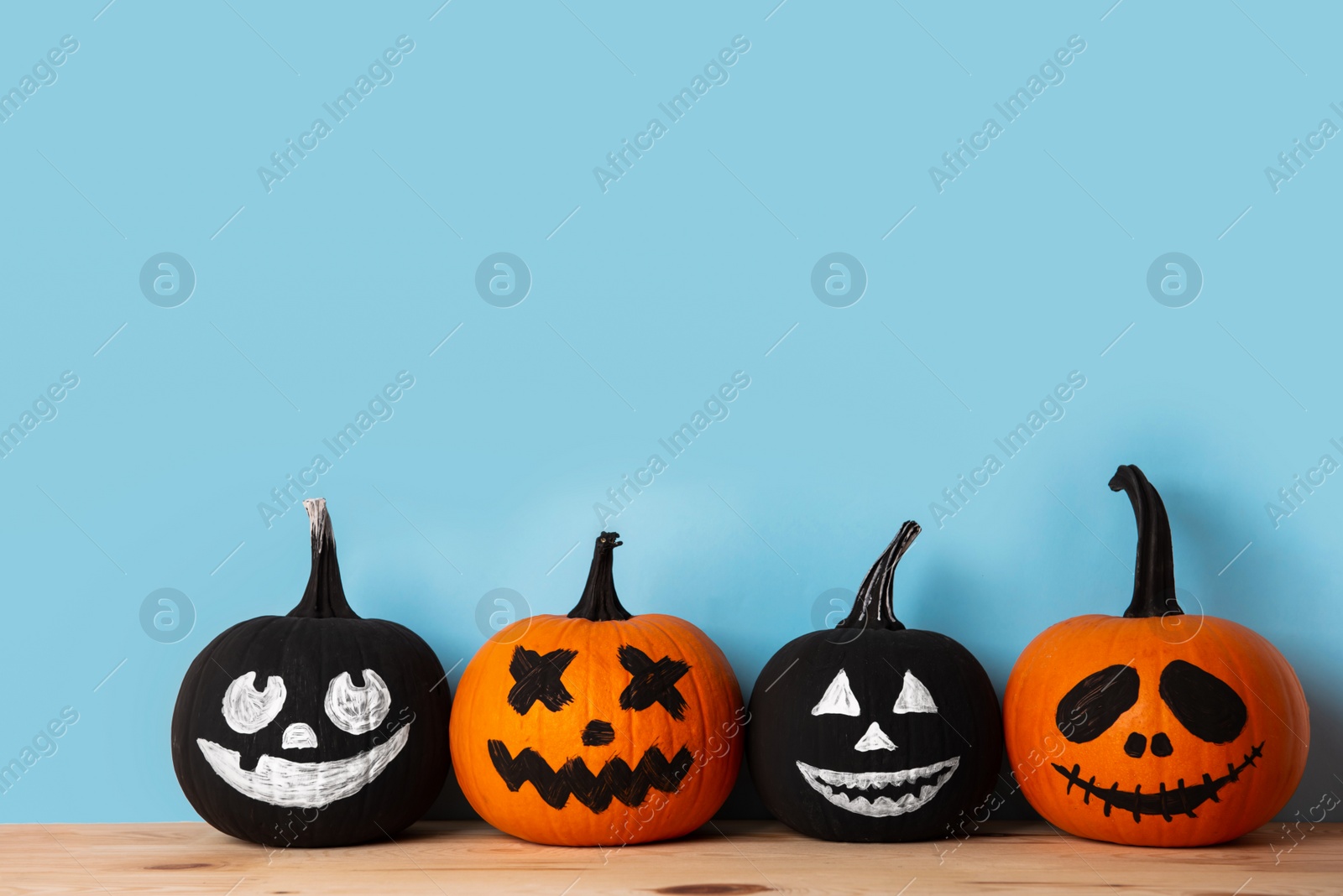 Photo of Halloween celebration. Pumpkins with spooky drawn faces on wooden table, space for text