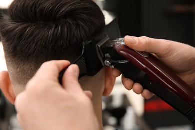 Photo of Professional barber making stylish haircut in salon, closeup