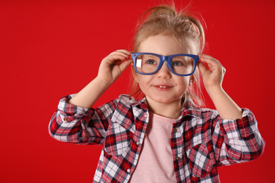 Photo of Funny little girl with glasses on red background. April fool's day