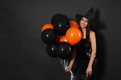 Photo of Beautiful woman wearing witch costume with balloons for Halloween party on black background, space for text