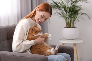 Happy woman with her cute cat in armchair at home