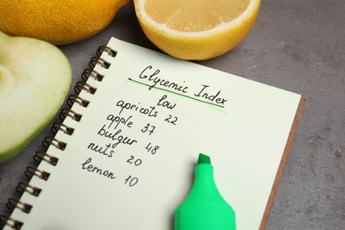 Photo of Notebook with products of low glycemic index, marker and fruits on grey table, closeup