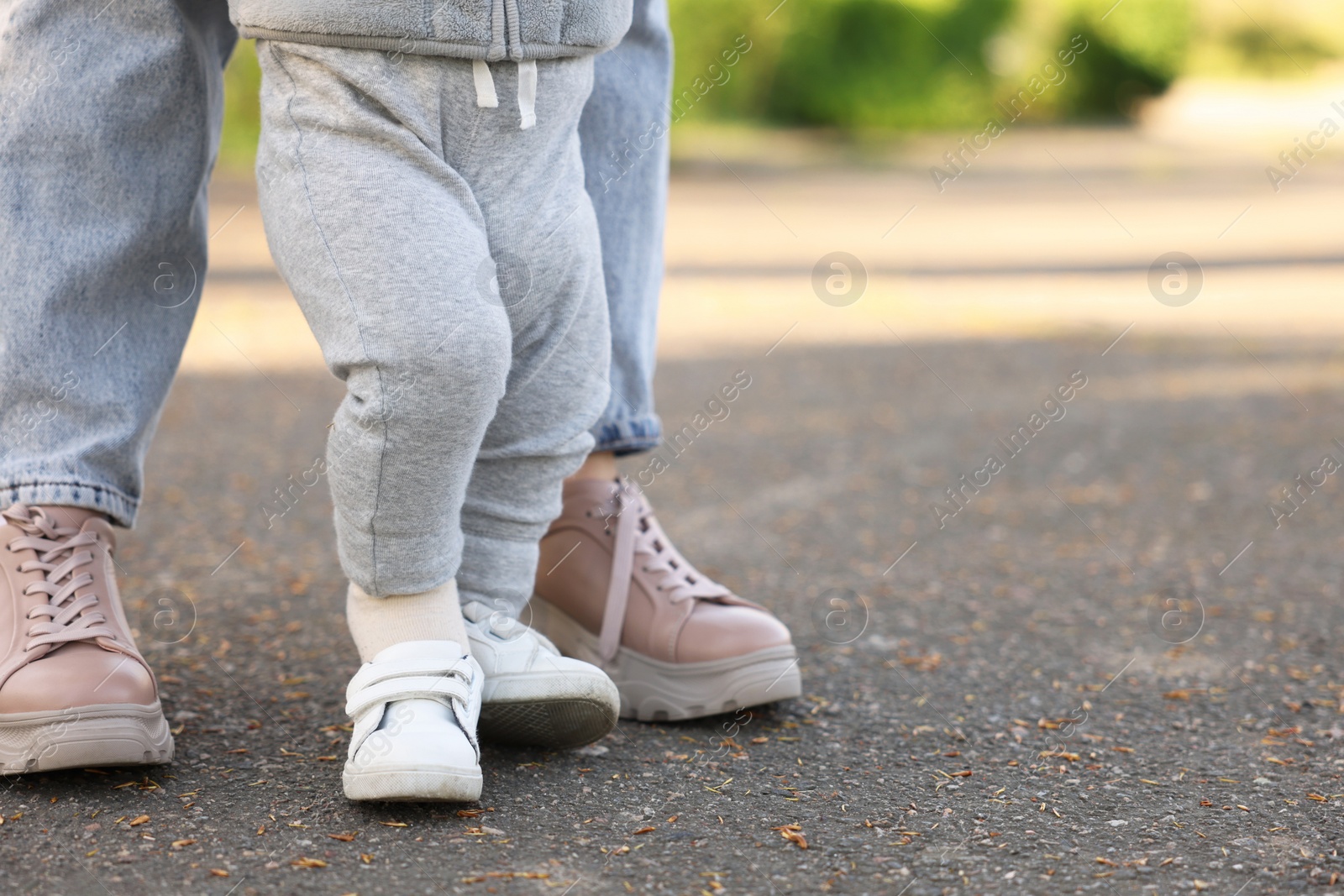 Photo of Mother teaching her baby how to walk outdoors, closeup. Space for text