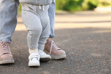 Mother teaching her baby how to walk outdoors, closeup. Space for text