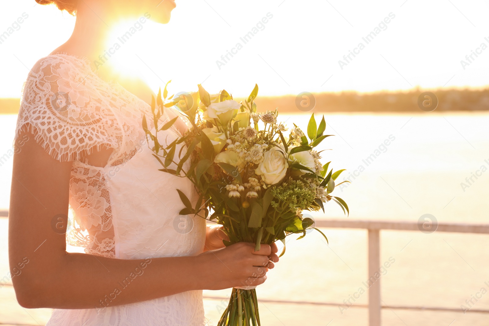 Photo of Bride in beautiful wedding dress with bouquet near river on sunset, closeup