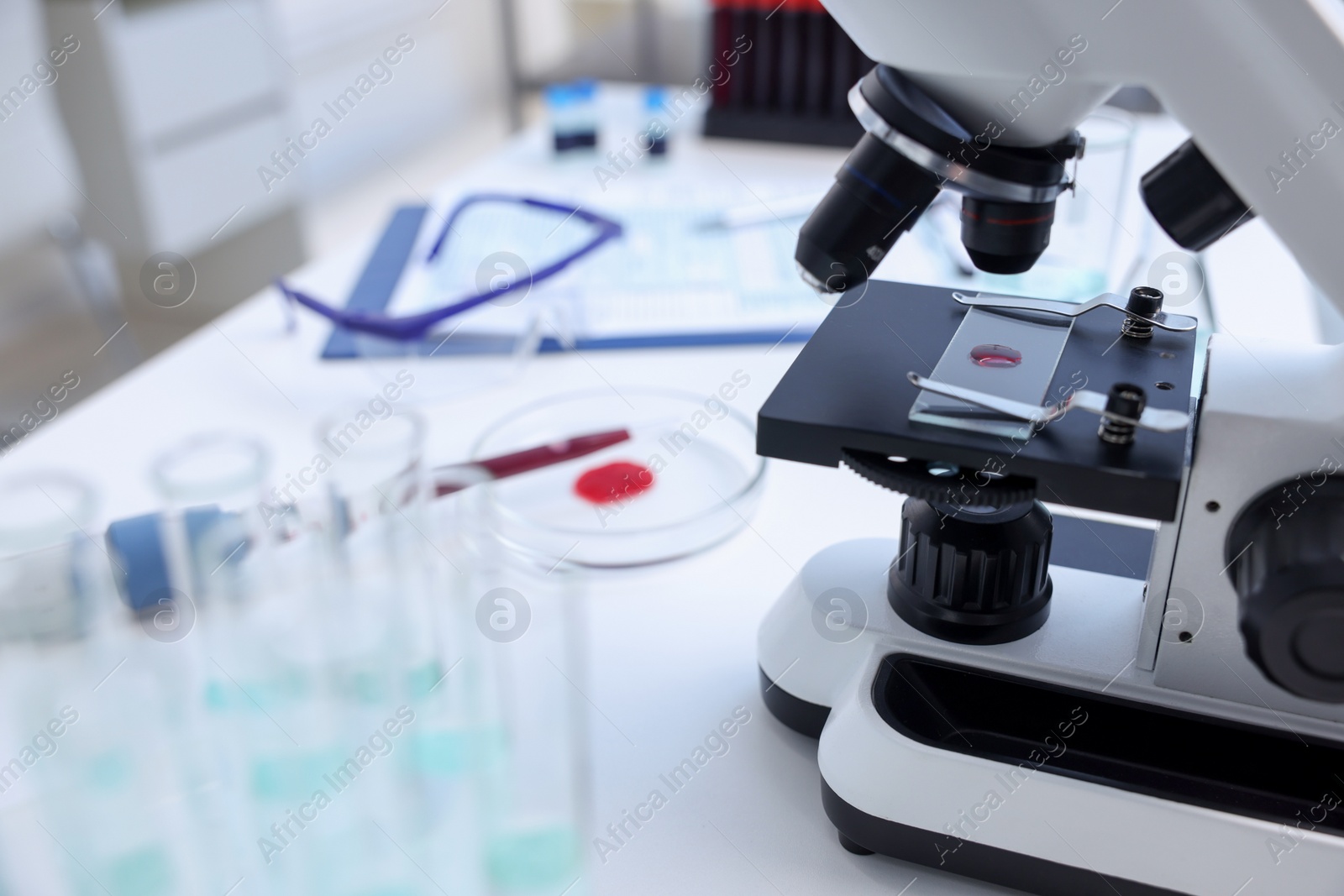 Photo of Modern medical microscope with sample of red liquid on white table in laboratory, closeup