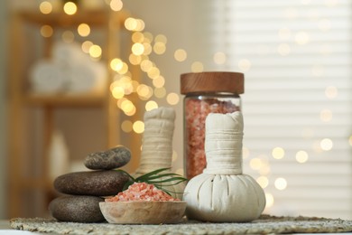 Photo of Spa composition. Herbal bags, sea salt and stones on table indoors, bokeh effect