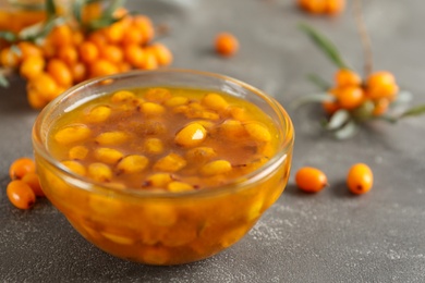 Photo of Delicious sea buckthorn jam and fresh berries on grey table, closeup