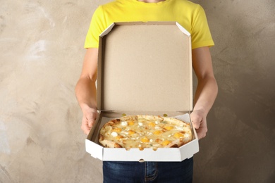 Young man with opened pizza box on color background. Food delivery service