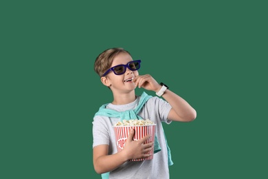 Cute boy in 3D glasses with popcorn bucket on color background