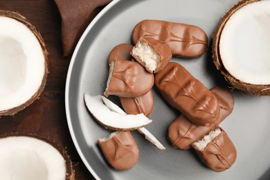 Photo of Delicious milk chocolate candy bars with coconut filling on wooden table, flat lay