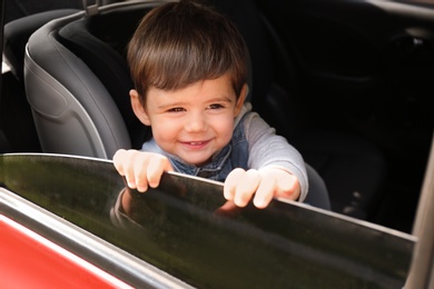 Photo of Cute little child sitting in safety seat inside car. Danger prevention