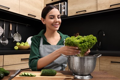 Woman in apron taking lettuce from colander at wooden table indoors