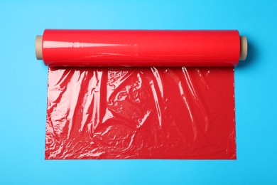 Photo of Roll of red plastic stretch wrap on light blue background, top view