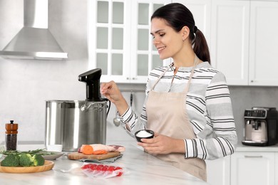 Photo of Woman salting products near pot with sous vide cooker at table in kitchen. Thermal immersion circulator