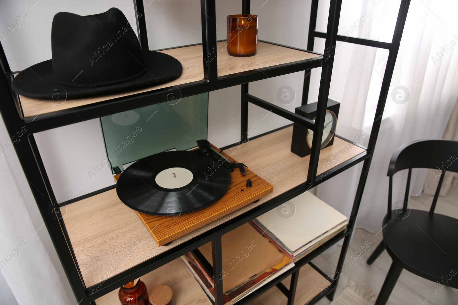 Photo of Stylish turntable with vinyl record on shelving unit indoors