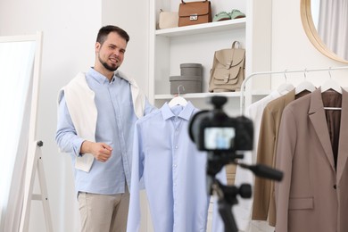 Photo of Smiling fashion blogger showing clothes while recording video at home