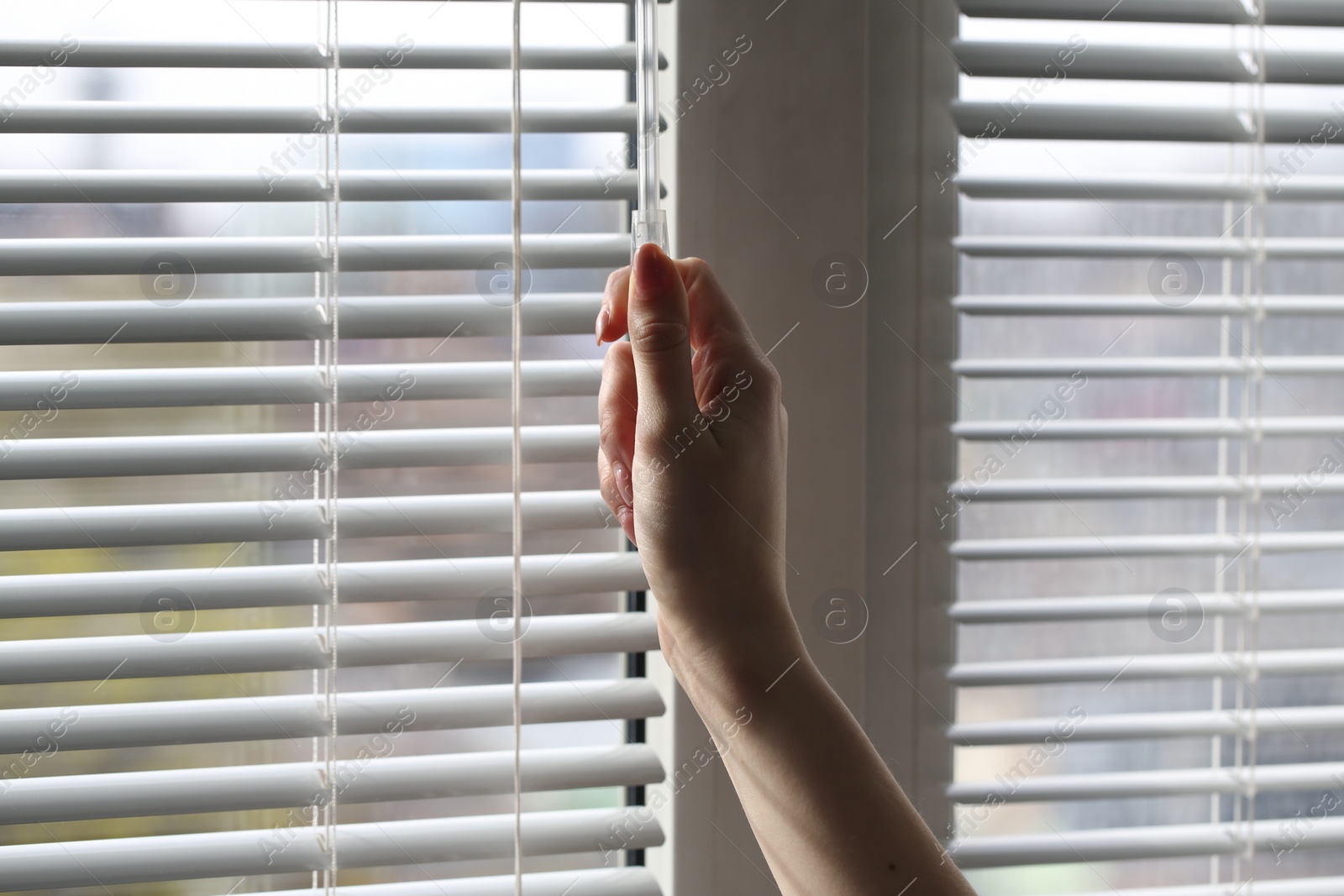 Photo of Woman opening white blinds at home, closeup