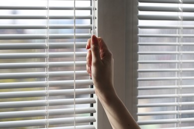 Woman opening white blinds at home, closeup