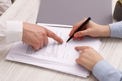 Photo of Man pointing at document and woman putting signature at wooden table, closeup