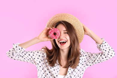 Beautiful young woman wearing stylish hat with donut on light pink background