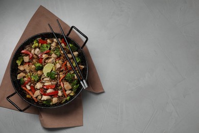 Photo of Stir-fry. Tasty noodles with meat in wok and chopsticks on grey textured table, top view. Space for text
