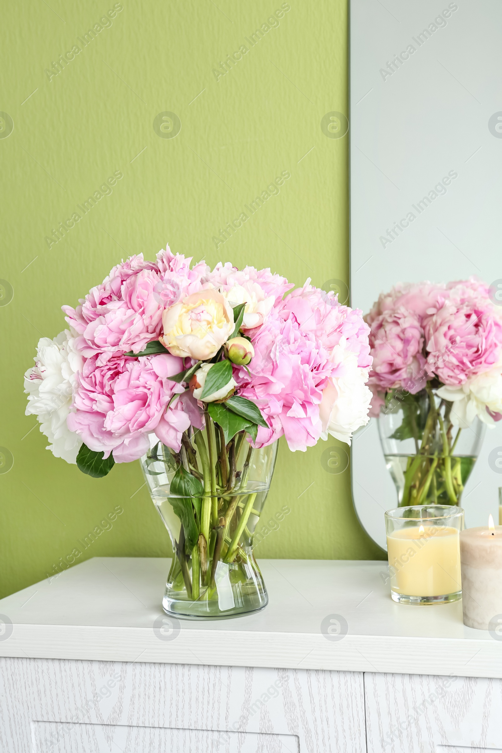 Photo of Beautiful peonies and candles on white dressing table near green wall