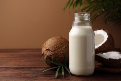 Photo of Glass bottle of delicious vegan milk, coconuts and palm leaves on wooden table, space for text