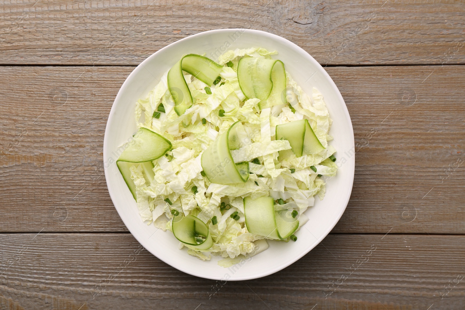 Photo of Tasty salad with Chinese cabbage, cucumber and green onion in bowl on wooden table, top view