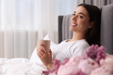 Photo of Happy woman with cup of drink in bed at home, space for text. Lazy morning